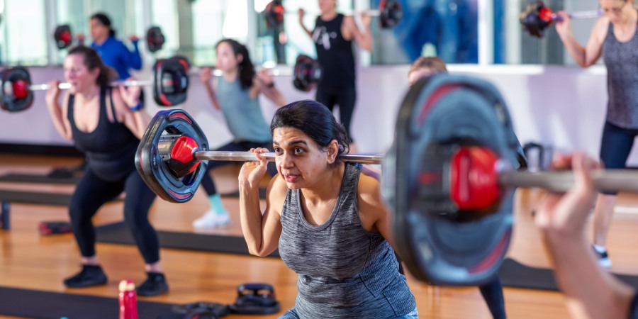 Poeple in a gym holding barbells over their shoulders during a group fitness class