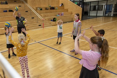Group of children learn how to pass the volleyball at school holiday program