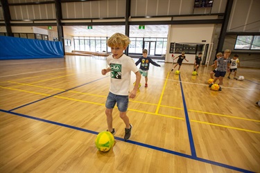 Children practise dribbling futsal balls during school holiday programs