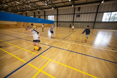 Group of holiday program children practise kicking the indoor soccer ball to each other