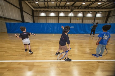 Little children practise hitting tennis balls with their racquet at the school holiday program