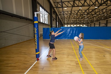A child attempts a Netball throw as another defends the net