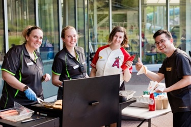 four people cooking sausages at a barbecue