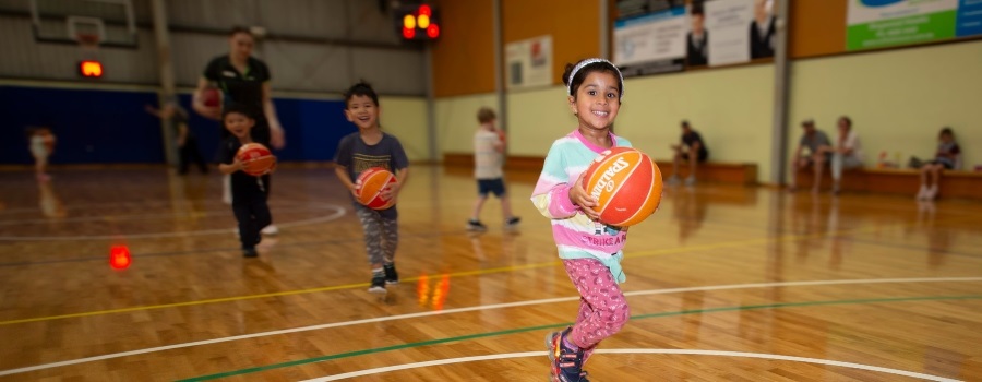 Young children running on basketball court holding basketballs 