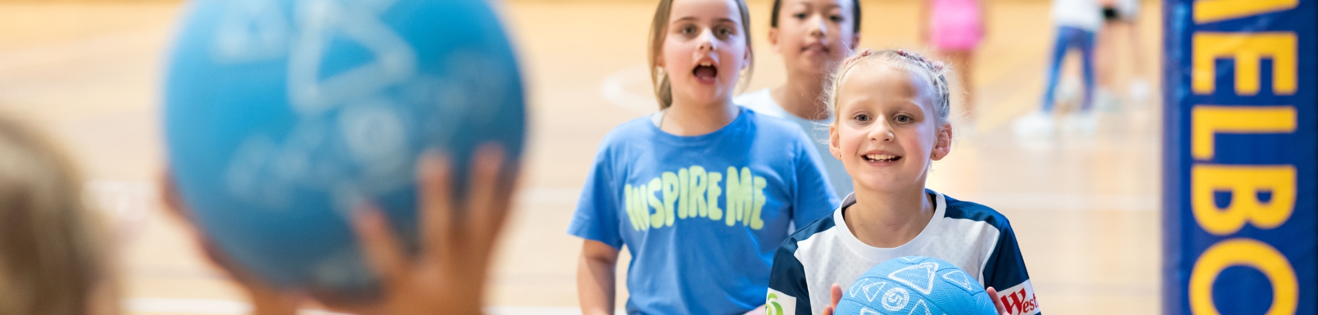 Young children take turns throwing netballs on an indoor court