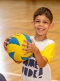 A young child smiles widely while hugging a volleyball