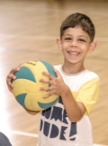 A young child smiles widely while hugging a volleyball